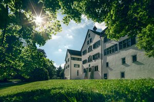 Aussenaufnahme Kloster Wettingen mit blauen Himmel, Sonne im Gegenlicht und einer grünen Wiese im Vordergrund.